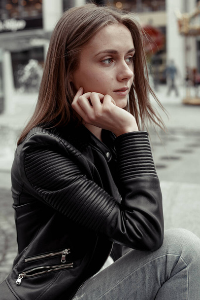 romantic young woman looking away. Female model wearing black leather jacket. The girl sitting on a bench  - Valokuva, kuva