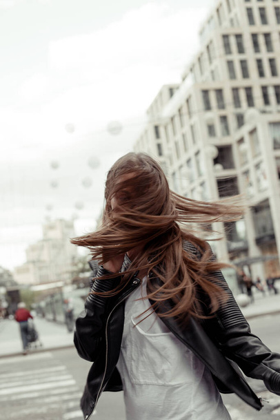 Kobieta trzęsie włosami na świeżym powietrzu. Młoda kobieta w czarnej skórzanej kurtce - Zdjęcie, obraz