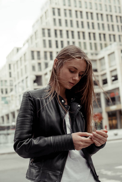 Woman write a phone message. Young blonde woman standing on urban background and using the smartphone - Fotografie, Obrázek