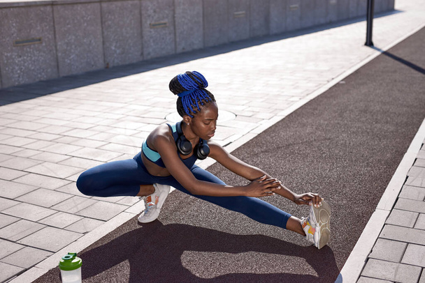 young woman stretching legs outdoors, enjoying daily routine warming up before running - Foto, imagen