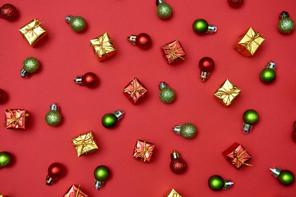Creative Christmas pattern with red and green shiny baubles and gifts on red background, copy space. Minimal, winter, new year concept. Top view, flat lay - Φωτογραφία, εικόνα
