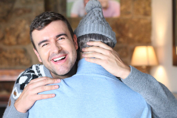 close-up portrait of handsome young man embracing male mannequin in wool hat and turtleneck sweater at home  - Photo, Image