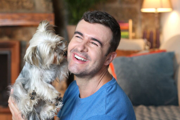 close-up portrait of handsome young man cuddling with little puppy at home  - Photo, Image