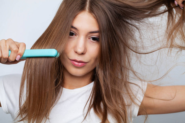 Женщина с красивыми длинными прямыми волосами с помощью выпрямителя для волос - Фото, изображение