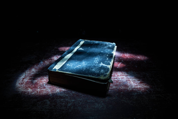 A stack of old books. Vintage book on wooden table. Magic lightning around a glowing book in the room of darkness. Selective focus - 写真・画像