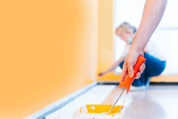 Pintura de uma parede laranja com um rolo e escova. Homem e mulher fazendo reformas. - Foto, Imagem