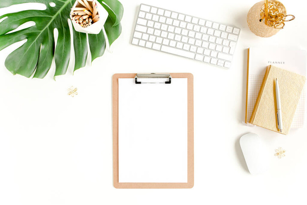 Flat lay home office desk. Female workspace with computer, clipboard, tropical palm leaves Monstera, accessories on white background. Top view.  - Фото, изображение