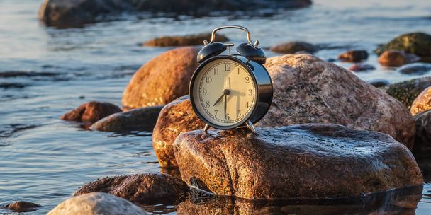Een klok die symbool staat voor de gouden eeuw van de fotografie die door de Zweedse Oostzee tijdens zonsondergang, wanneer de zomer wordt herfst, en sommige landen zullen binnenkort wenden tot de wintertijd. - Foto, afbeelding
