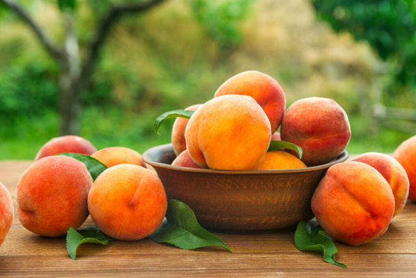 熟したおいしいとジューシーな桃は庭の木製のテーブルの上に皿の上にあります。木のテーブルの上に新鮮な甘い桃,選択的な焦点. - 写真・画像