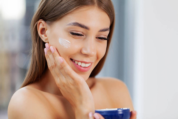 Laughing girl applying moisturizing cream on her face. - Fotografie, Obrázek