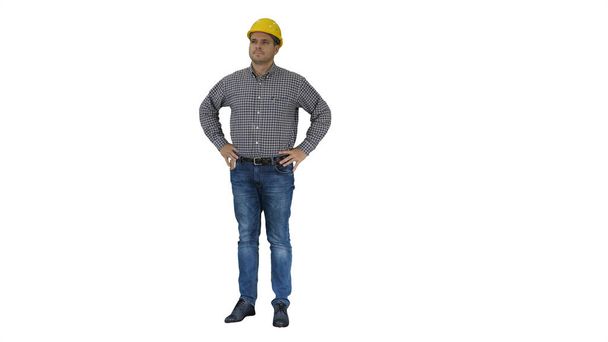 Obrero de la construcción sonriente en casco amarillo mirando el objeto perfecto bien construido Manos en las caderas sobre fondo blanco. - Foto, imagen