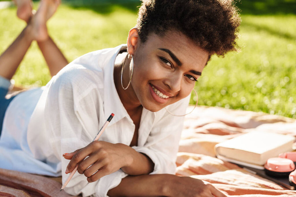 Attractive smiling young african womam writing in a diary in the park - Foto, imagen