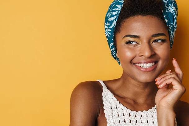 Imagen de la divertida mujer afroamericana posando y sonriendo sobre una cámara aislada de fondo amarillo - Foto, imagen