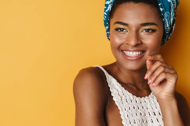 Imagen de la divertida mujer afroamericana posando y sonriendo sobre una cámara aislada de fondo amarillo - Foto, Imagen