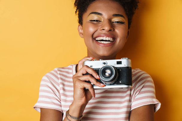 Image of laughing african american woman taking photo on retro camera isolated yellow background - Photo, image