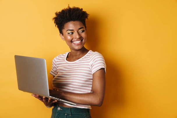 Image of joyful african american woman smiling and using laptop isolated yellow background - Φωτογραφία, εικόνα