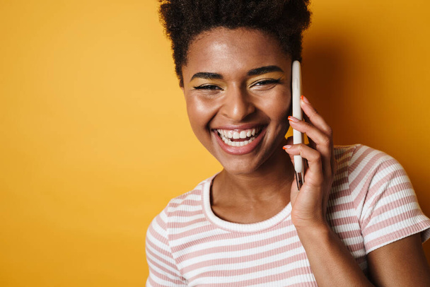 Image of joyful african american woman laughing and talking on mobile phone isolated yellow background - Foto, Imagem
