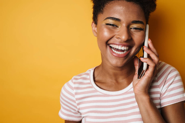 Image of joyful african american woman laughing and talking on mobile phone isolated yellow background - Fotografie, Obrázek