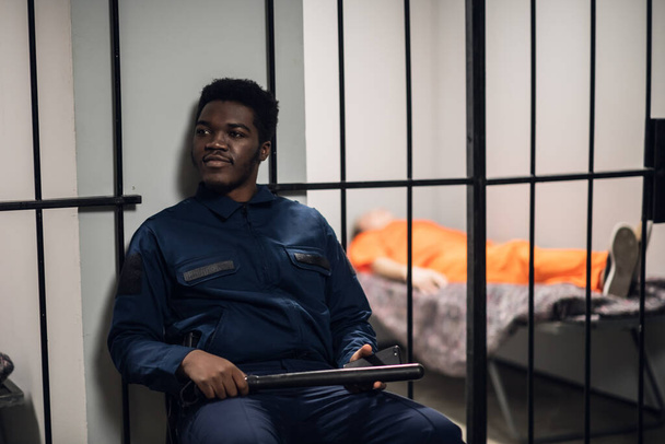 Silny czarny strażnik więzienny strzeże cel z więźniami w korytarzu więziennym - Zdjęcie, obraz