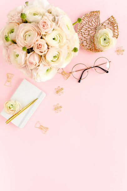 Stylized, pink womens home office desk. Workspace with bouquet ranunculus and roses, clipboard on pink background. Flat lay. Top view. - Foto, immagini