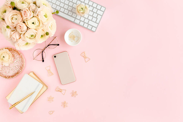 Stylized, pink womens home office desk. Workspace with computer, bouquet ranunculus and roses, phone on pink background. Flat lay. Top view. - Фото, зображення