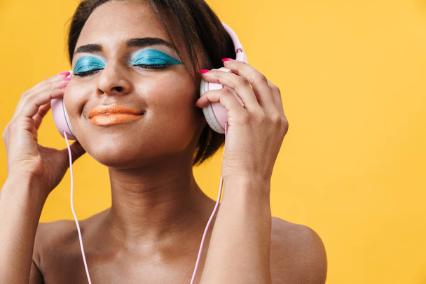 Image of shirtless african american woman smiling and using headphones isolated over yellow background - Φωτογραφία, εικόνα