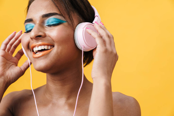 Image of shirtless african american woman laughing and using headphones isolated over yellow background - Foto, imagen