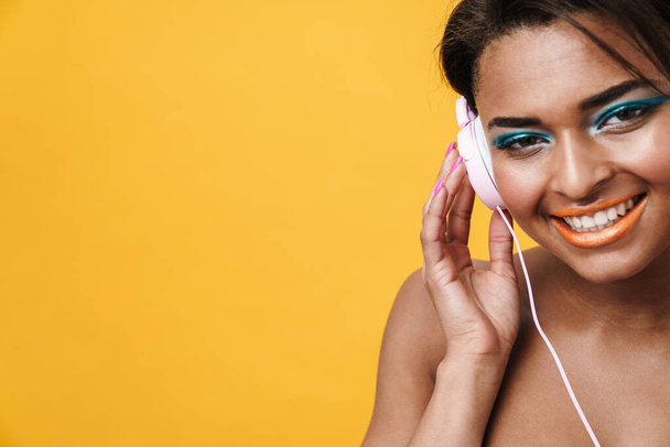 Image of shirtless african american woman laughing and using headphones isolated over yellow background - Foto, Bild