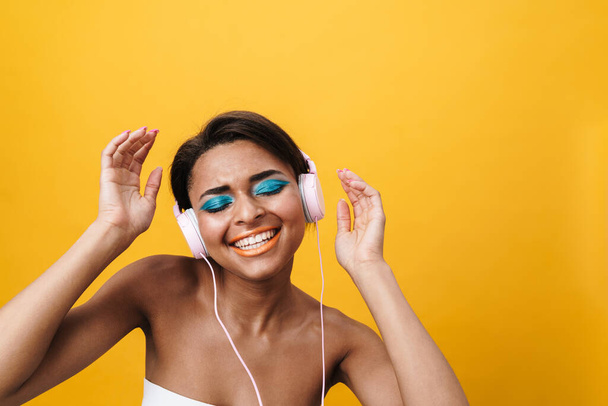 Image of shirtless african american woman singing and using headphones isolated over yellow background - Foto, immagini