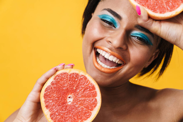 Image of shirtless african american woman laughing while posing with grapefruit isolated over yellow wall - Φωτογραφία, εικόνα