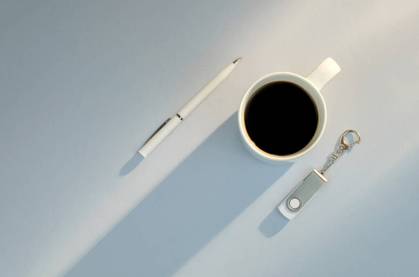 Flash drive, pen, cup of coffee on blue background with sun light - 写真・画像