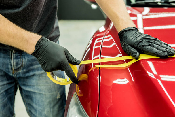 Car service worker applying protective tape on the car details before polishing. - Valokuva, kuva