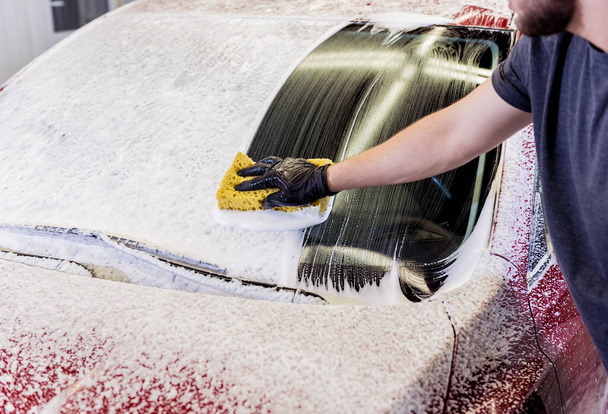 Worker washing red car with sponge on a car wash - 写真・画像