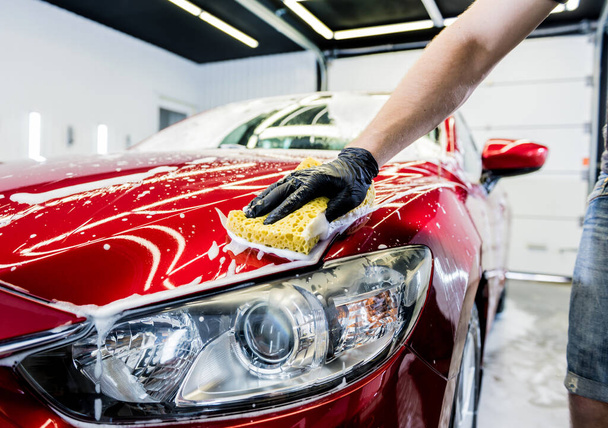 Worker washing red car with sponge on a car wash - Foto, imagen