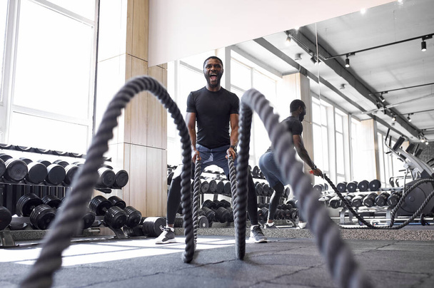 afro athlete doing battle ropes exercise in gym - 写真・画像