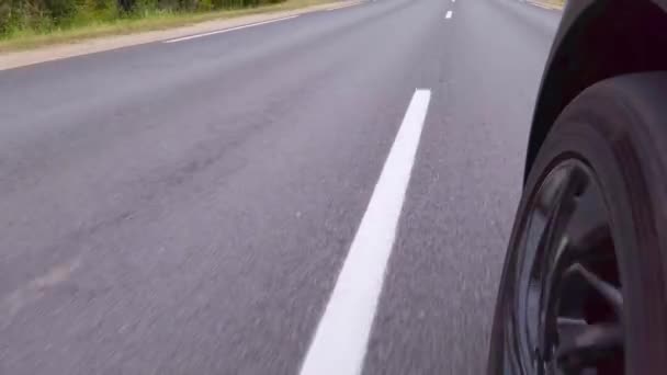 Lage hoek POV van de voorste auto wiel. Een asfaltweg met witte scheidingslijnen. - Video