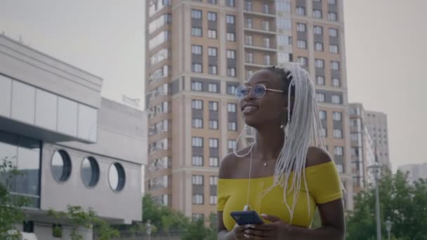 Czarna dziewczyna nosi słuchawki na zewnątrz - Materiał filmowy, wideo