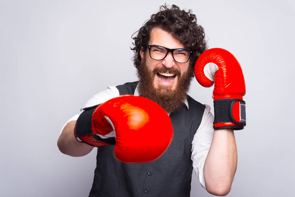Photo d'un homme barbu portant un costume et frappant avec des gants de boxe - Photo, image