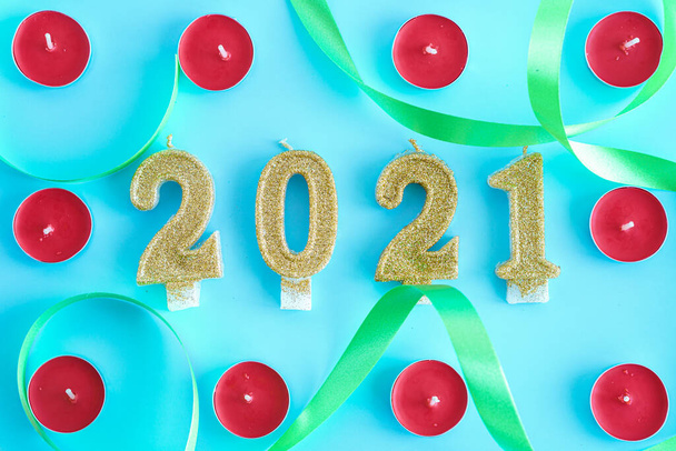 Xmas, winter, new year concept - Blue Christmas background with frame of little round red candles and gold numbers 2021 in center entwined with green ribbon. Flatly, top view, overhead. Copy space - Fotó, kép