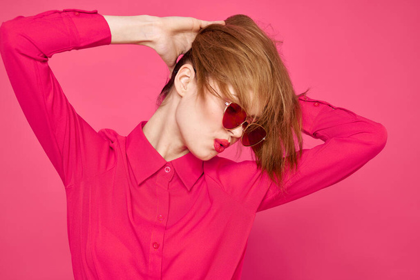 Cheerful woman in sunglasses touching hair with hands and pink shirt cropped view - Foto, immagini