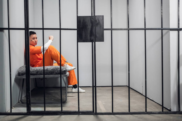 Celda solitaria con un criminal con una bata naranja en una prisión asiática. Copiar espacio. Emociones tristes de un joven. - Foto, imagen