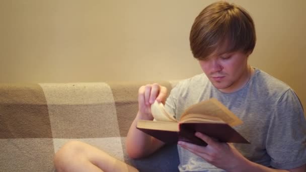 Student prepares for the exams at home. Concept. Frightened young man turning pages of an old book very fast, trying to find information with panic in his eyes. - Footage, Video