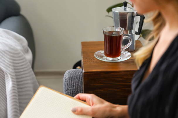 Donna con tazza di caffè libro di lettura sul divano a casa - Foto, immagini