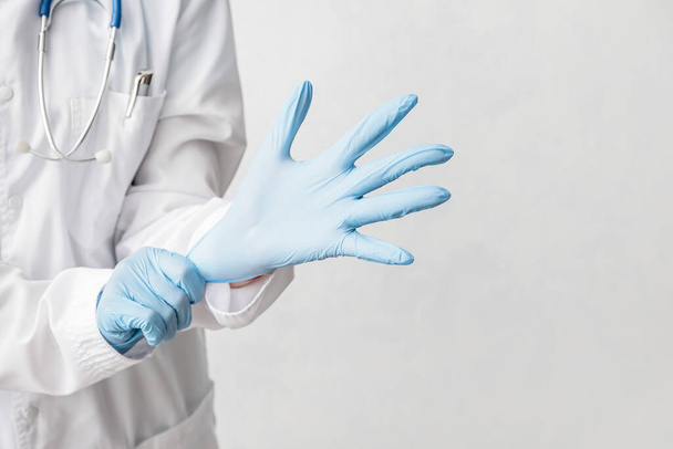 Doctor putting on medical gloves against light background - Photo, Image
