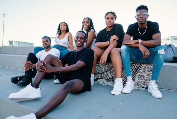 Grupo de jóvenes amigos negros africanos modernos felizmente sentados juntos - Foto, Imagen