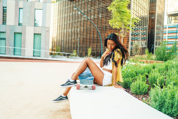 bonita chica atlética sentada con un longboard en la ciudad moderna - Foto, imagen