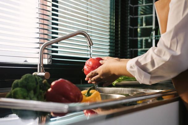 Aasian kädet nainen pesee vihanneksia paprika ja valmistelu terveellistä ruokaa keittiössä. - Valokuva, kuva