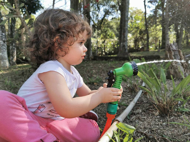 Cute brazylijski dziewczynka zabawy z wężem wodnym w ogrodzie. - Zdjęcie, obraz