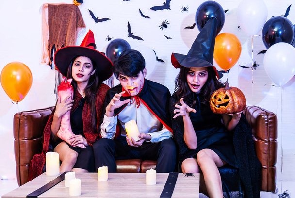 Asian Happy friends sitting on sofa in costumes and makeup on a celebration of Halloween posing with pumpkin and fake human leg in party, Group of young people enjoying Halloween party with many items at home or nightclub. - Photo, Image
