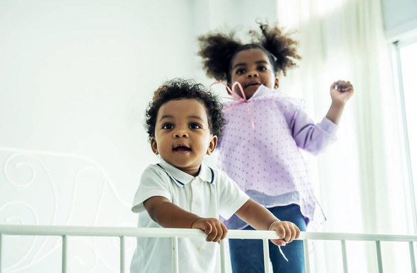 Happy African American naughty kids boy and girl jumping on the bed with happiness.two funny small energy mixed race children brother with sister having fun play on bed - Foto, Bild